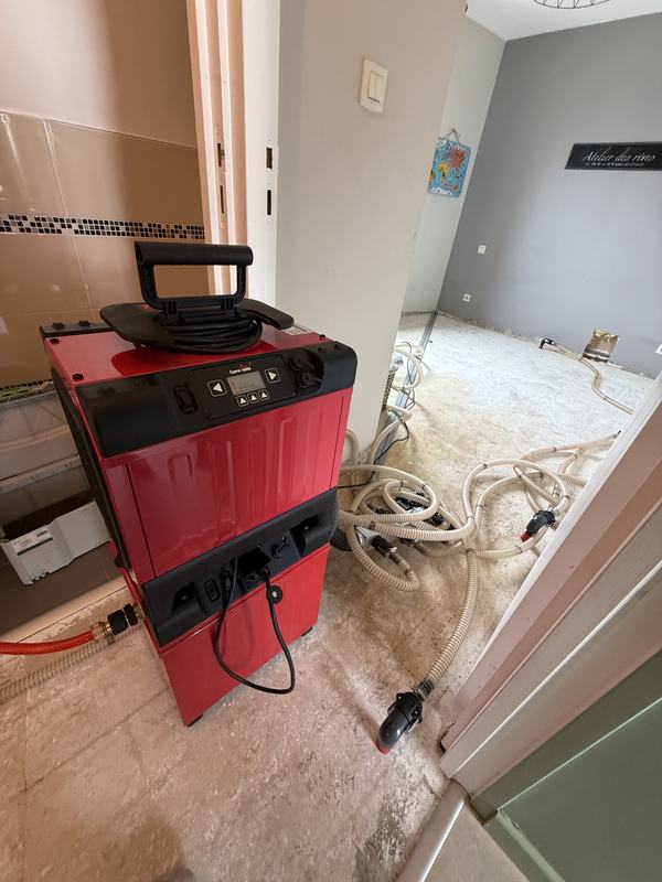 Déshumidificateur Corroventa raccordé par tuyaux souples pour l'assèchement d'une chape en salle de bain